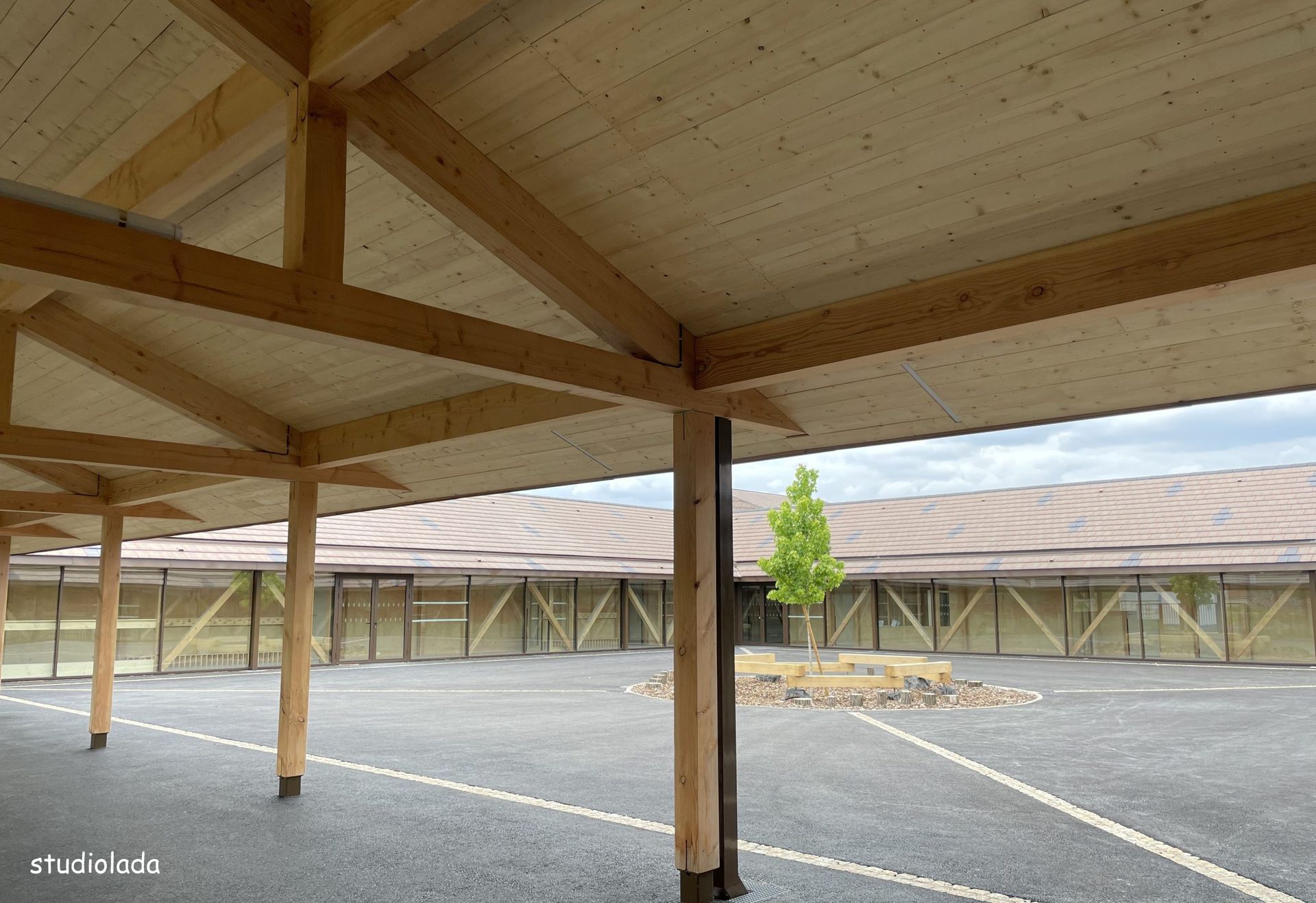 Abri en bois aux poutres apparentes, donnant sur une cour intérieure avec des bâtiments en arrière-plan.