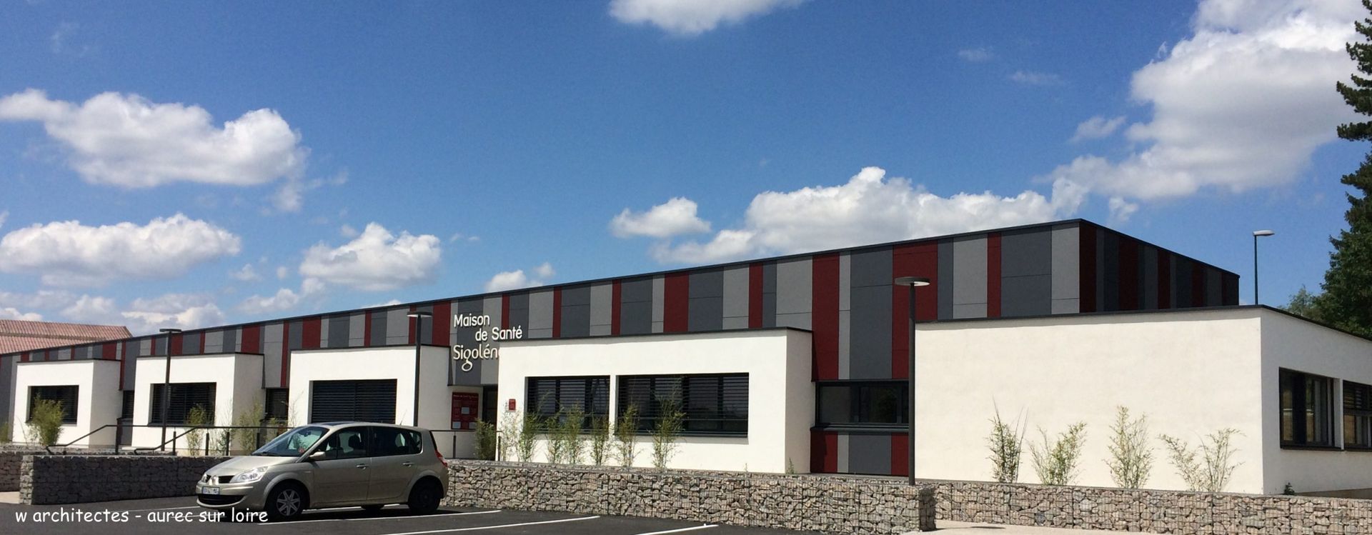 Vue extérieure d'un bâtiment moderne avec une voiture garée devant par une journée ensoleillée.