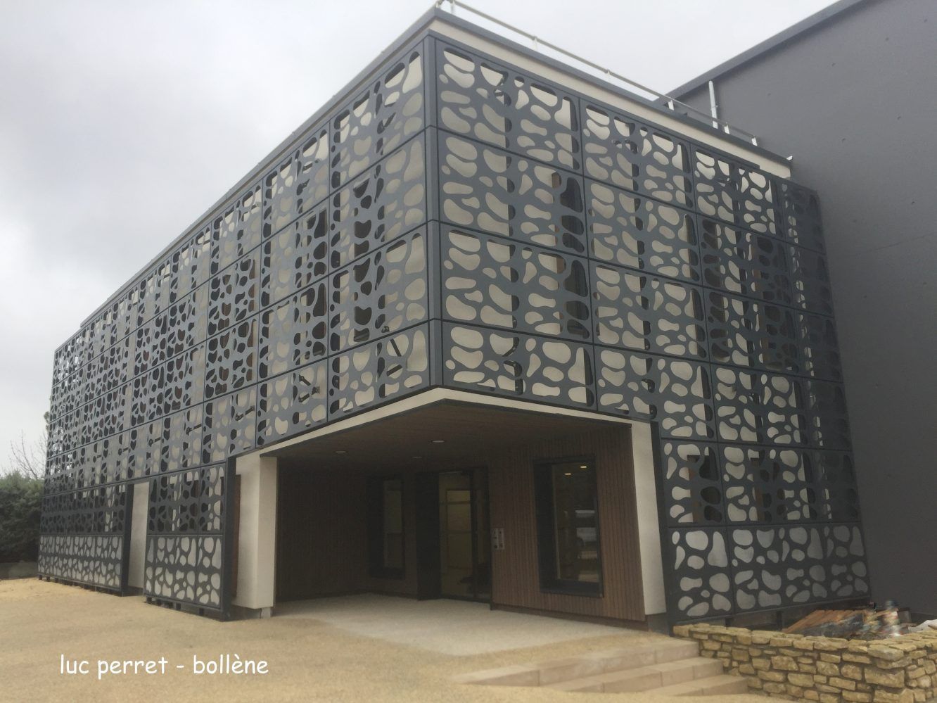 Bâtiment moderne à façade métallique sombre ornée de motifs au-dessus des baies vitrées.