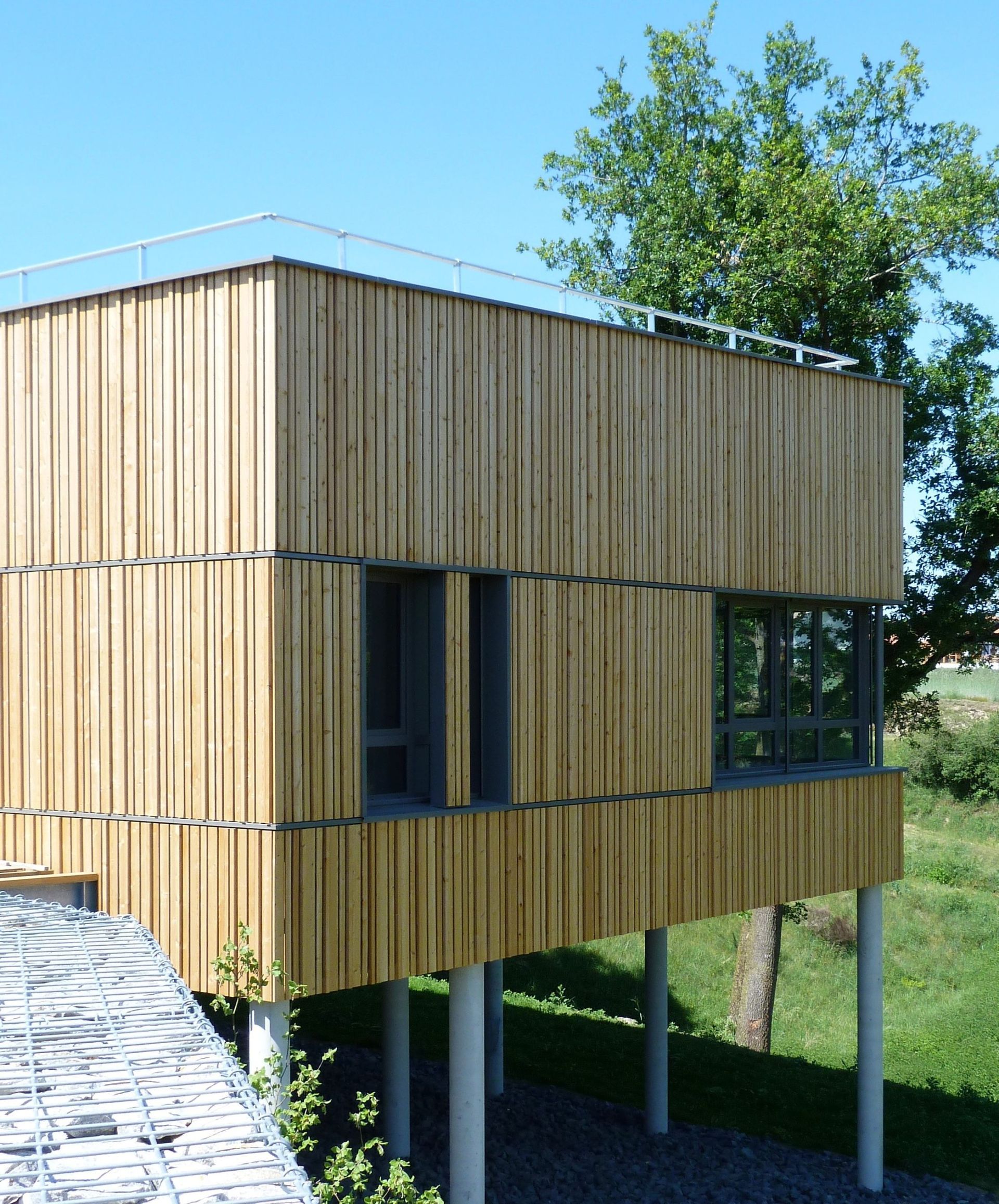 Bâtiment moderne en bois sur pilotis, avec fenêtres et rambarde sur le toit.