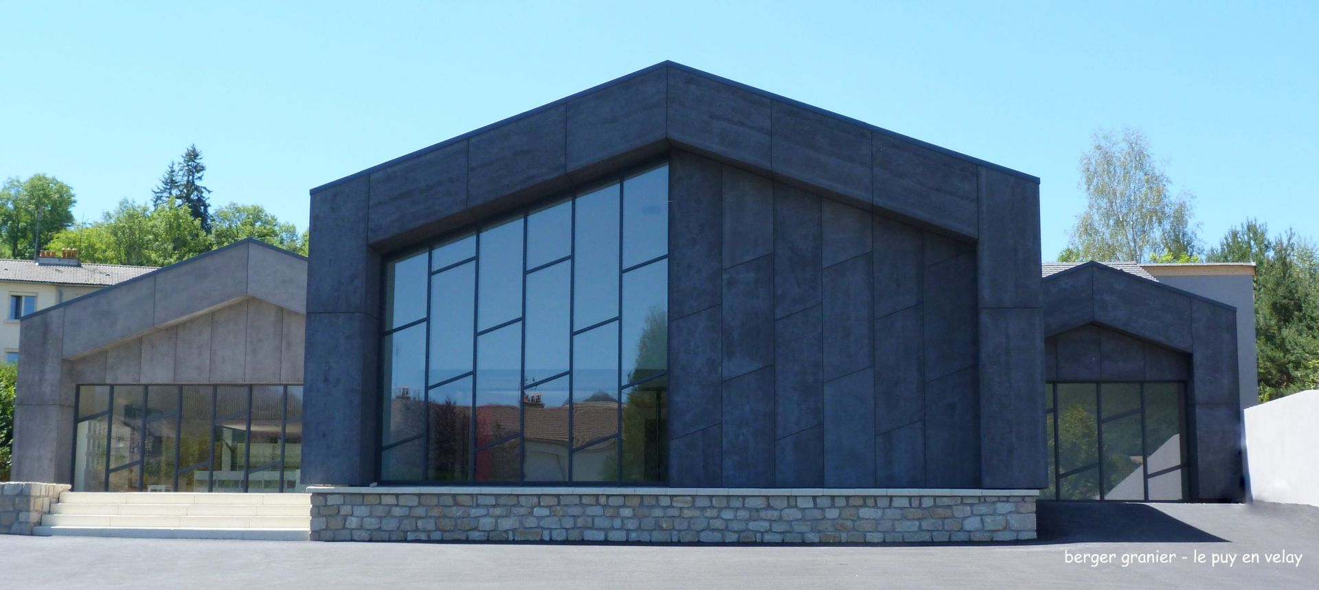 Bâtiment moderne avec des fenêtres en verre, des murs gris et un ciel bleu.