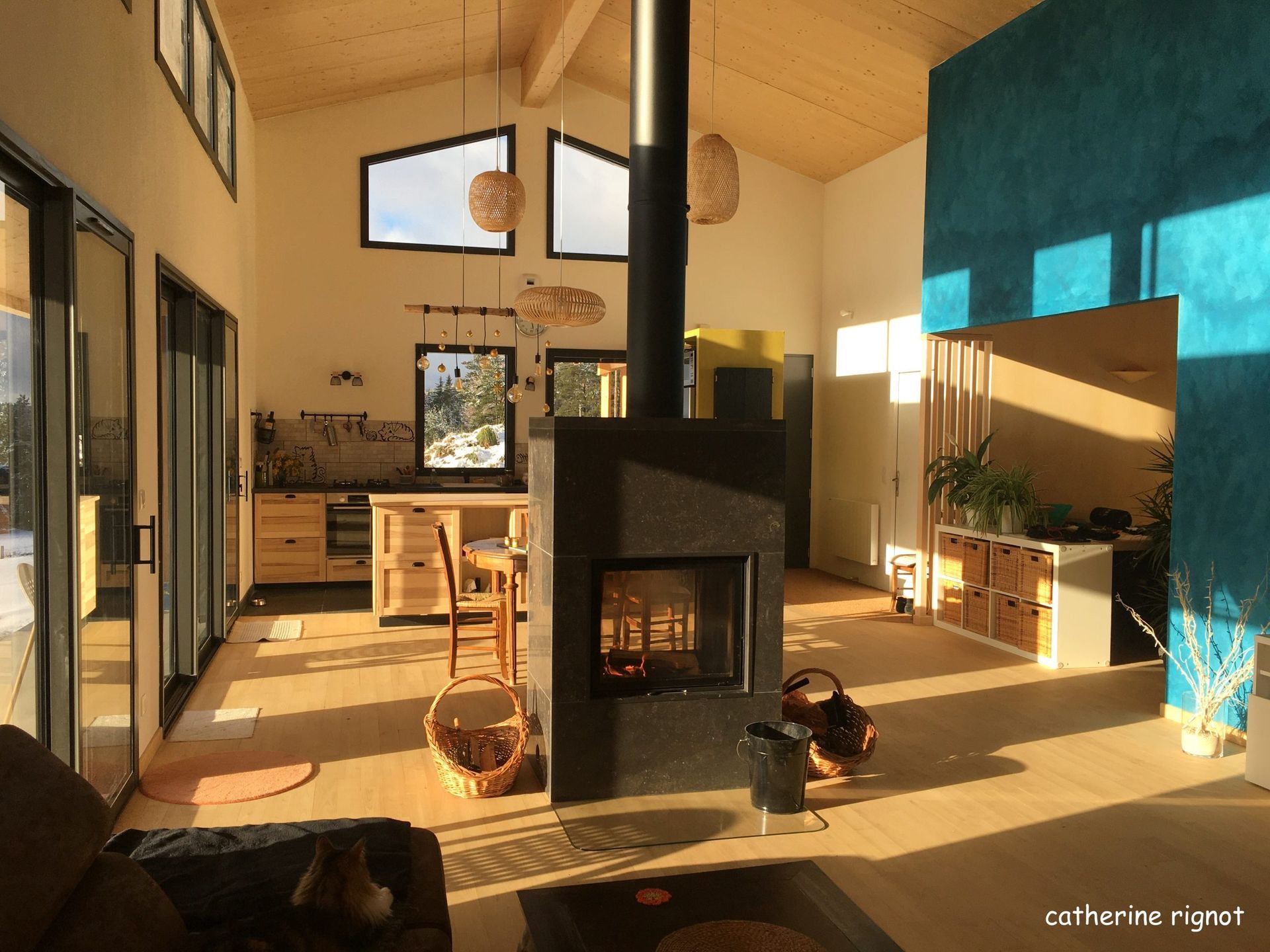 Intérieur lumineux avec cheminée, cuisine et grandes fenêtres ; lumière naturelle.