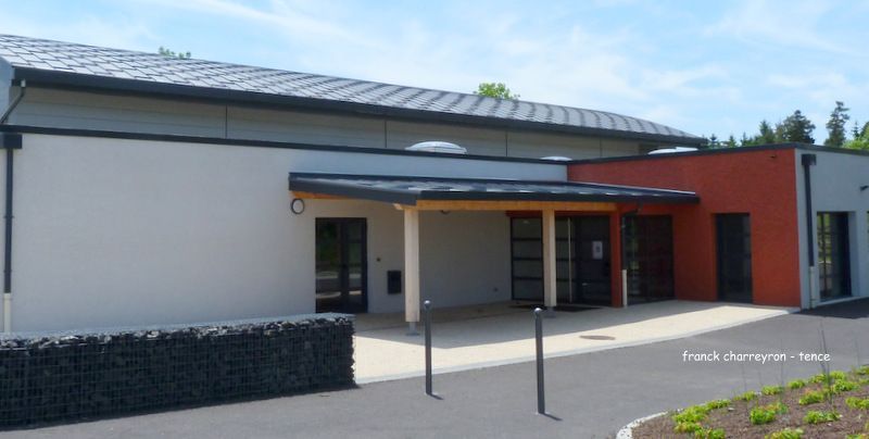 Bâtiment moderne aux murs gris et rouges, toit noir et auvent d'entrée.