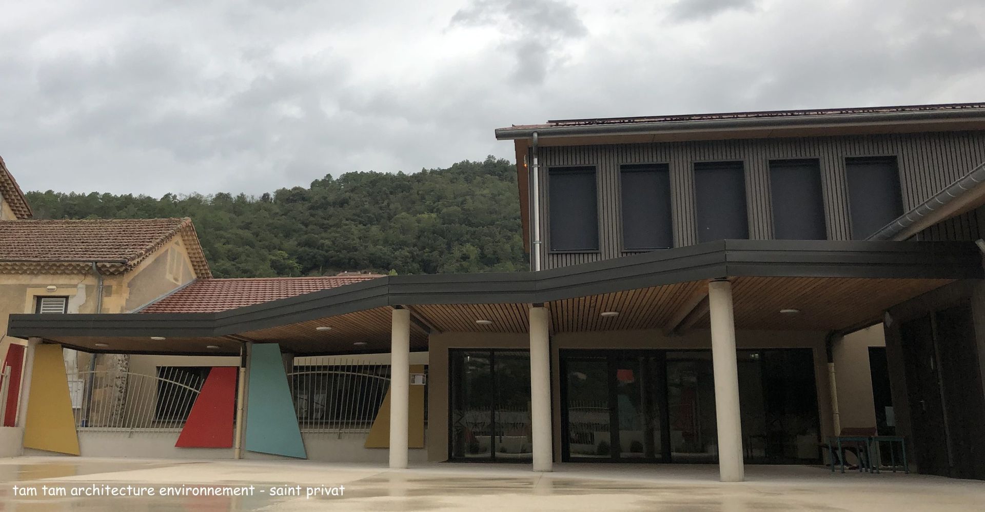 Extérieur de l'école avec entrée couverte et touches de couleur, sous un ciel couvert.