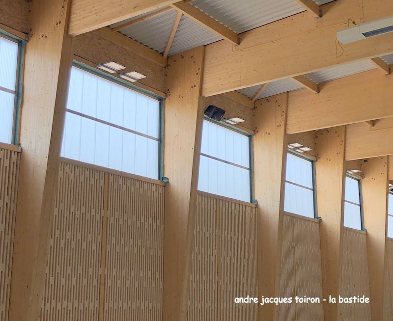 Vue intérieure d'un bâtiment aux poutres en bois clair et aux fenêtres à vitres translucides.