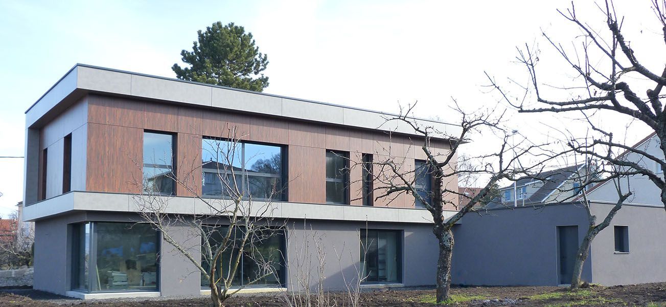 Maison moderne à deux étages avec bardage en bois et gris, grandes fenêtres et arbres dénudés devant.