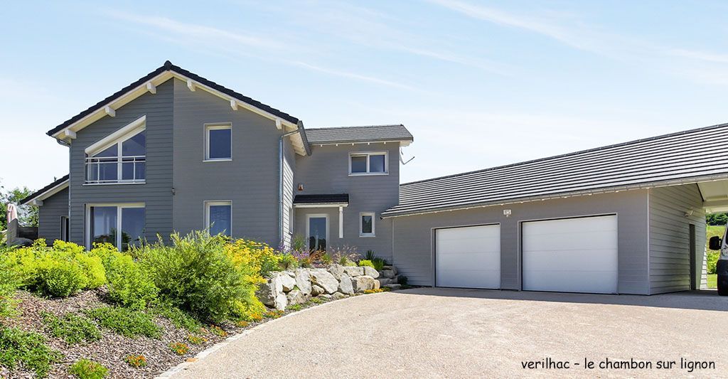 Maison grise à deux étages avec garage attenant, allée en gravier et jardin paysager.