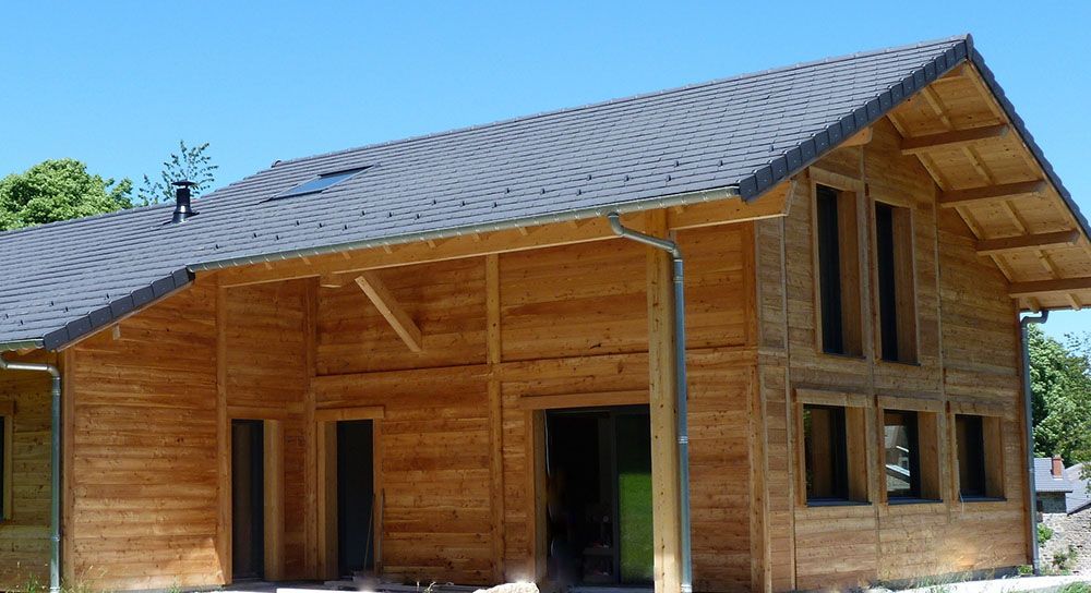 Maison en bois en construction, toit gris foncé, ciel bleu en arrière-plan.