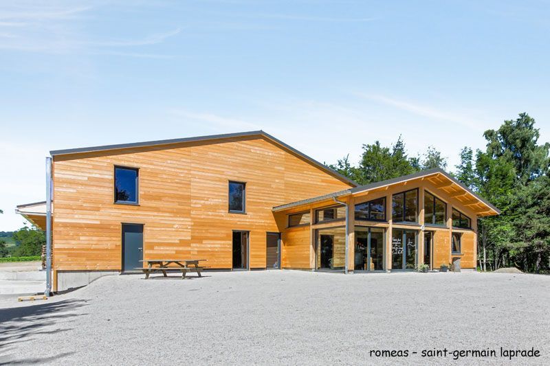 Bâtiment en bois avec façade vitrée et table de pique-nique, Saint-Germain-Laprade, France, sur un sol gravillonné.