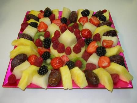 Variedad de frutas dispuestas en filas sobre una bandeja de color rosa brillante, entre las que se incluyen fresas, piña, uvas y melón.