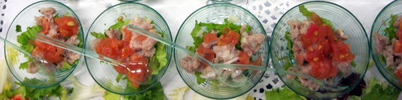 Cinco cuencos de cristal con ensalada picada de colores y hierbas sobre un mantel azul claro.
