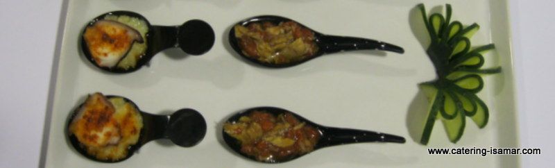 Dos filas de sartenes pequeñas con mango negro, con comida horneada junto a una guarnición verde en forma de flor.