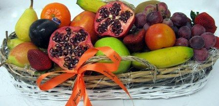 Fruta fresca variada en una cesta tejida con una cinta naranja sobre un fondo blanco.