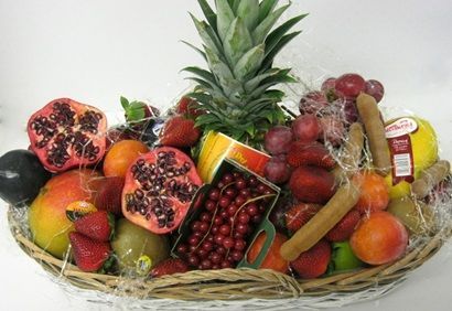 Cesta de frutas variadas con piña, granadas, uvas, plátanos, fresas y naranjas.