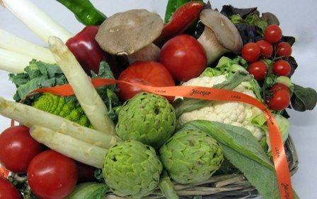 Surtido de verduras frescas y setas atadas con una cinta naranja en una cesta.
