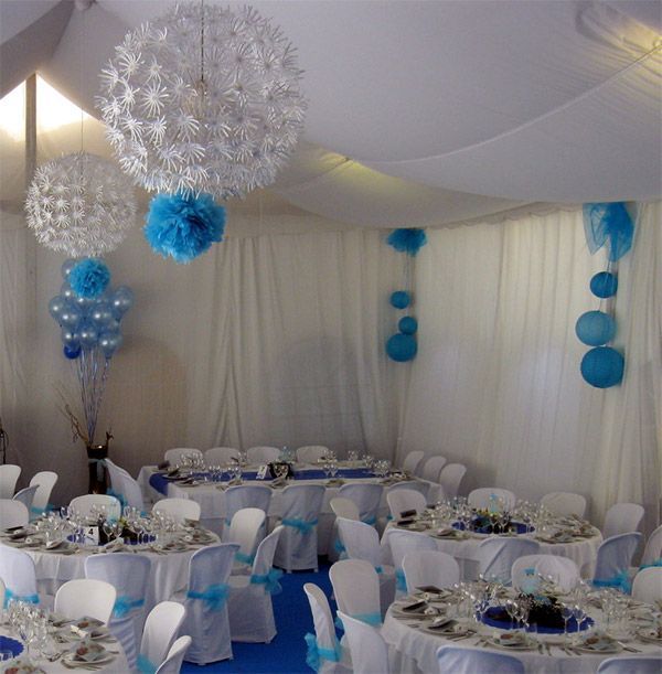 Salón de banquetes decorado en azul y blanco con mesas redondas, cortinas de tela y centros de mesa florales colgantes.