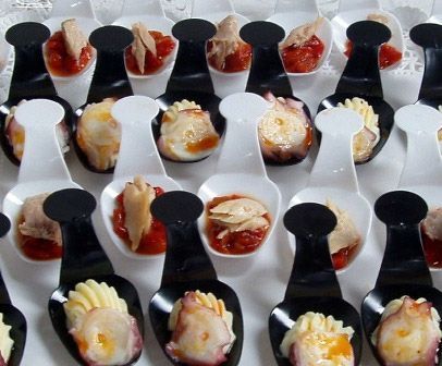 Filas de cucharitas de postre en miniatura coronadas con coloridos aperitivos del tamaño de un bocado en una bandeja.