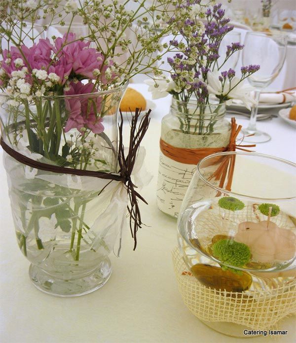 Jarrones de cristal con flores silvestres y rodajas de limón sobre una mesa decorada con colores vivos.