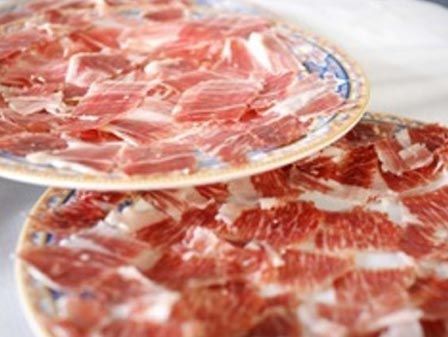 Platos de jamón curado cortado en lonchas finas, probablemente prosciutto, dispuestos sobre una mesa.