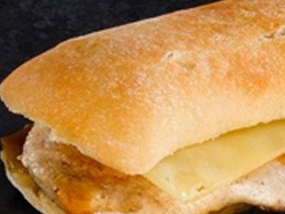 Primer plano de un sándwich con un pan crujiente, queso derretido y relleno de carne.