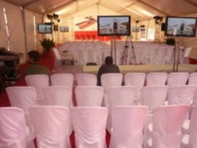 Carpa con filas de sillas blancas frente a un escenario y dos pantallas en la parte delantera.
