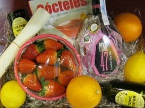 Una cesta de regalo con una selección de bebidas de frutas y chocolate, que incluye fresas, naranjas y una botella de licor rosa.
