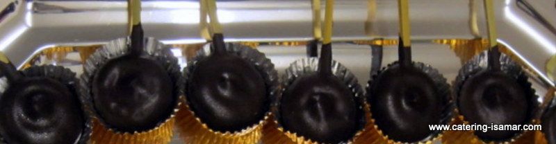 Hilera de tapas y sartenes negras colgadas en un estante de cocina, con ganchos y detalles de cadena de color dorado.