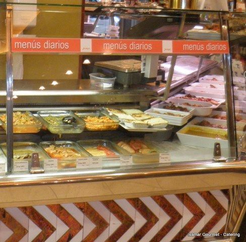 Mostrador de cristal para la exhibición de alimentos, con bandejas de platos preparados y un letrero que dice