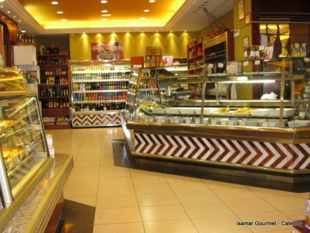 Interior de tienda gourmet con iluminación cálida, vitrinas de cristal y estantes con alimentos envasados.