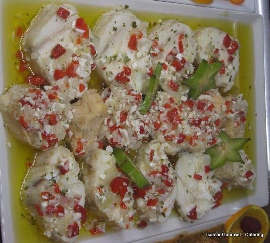 Bandeja de dumplings al vapor cubiertos con salsa cremosa, guarnición de pimiento rojo picado y trozos de pimiento verde.