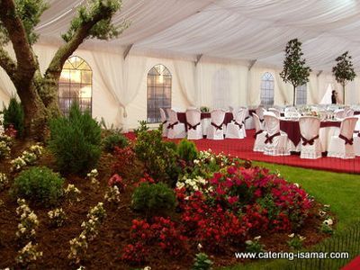 Carpa de banquete decorada con alfombra roja, sillas con fundas blancas y arreglos florales.