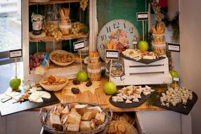 Exhibición rústica de panadería con panes, pasteles, manzanas verdes y un gran reloj al fondo.