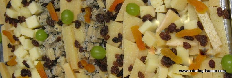 Surtido de lonchas de queso cubiertas con uvas, pasas y frutos secos, dispuestas en una bandeja de aperitivos (primer plano).