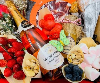Cesta de regalo con fresas, bombones, frutos secos y una botella de champán en un arreglo festivo.