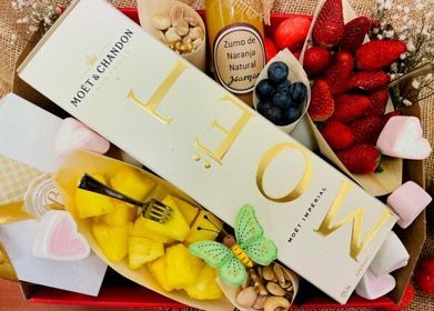 Caja de regalo de lujo con champán, fruta, macarons y flores en un elegante empaque rosa y dorado.
