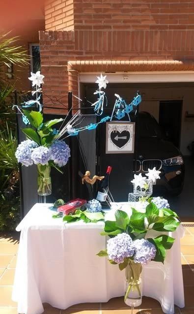 Mesa conmemorativa blanca con flores y adornos iluminados frente a una pared de ladrillos y una puerta.
