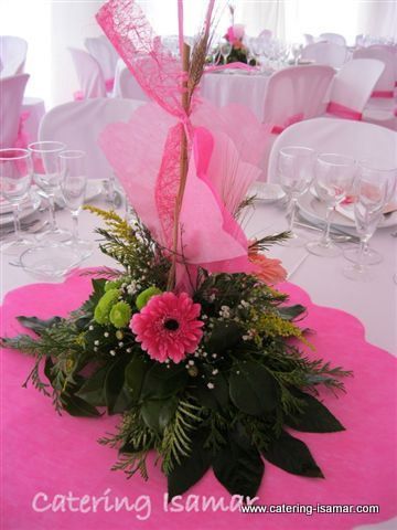 Centro de mesa floral rosa sobre una mesa de banquete decorada con sillas blancas y cristalería.