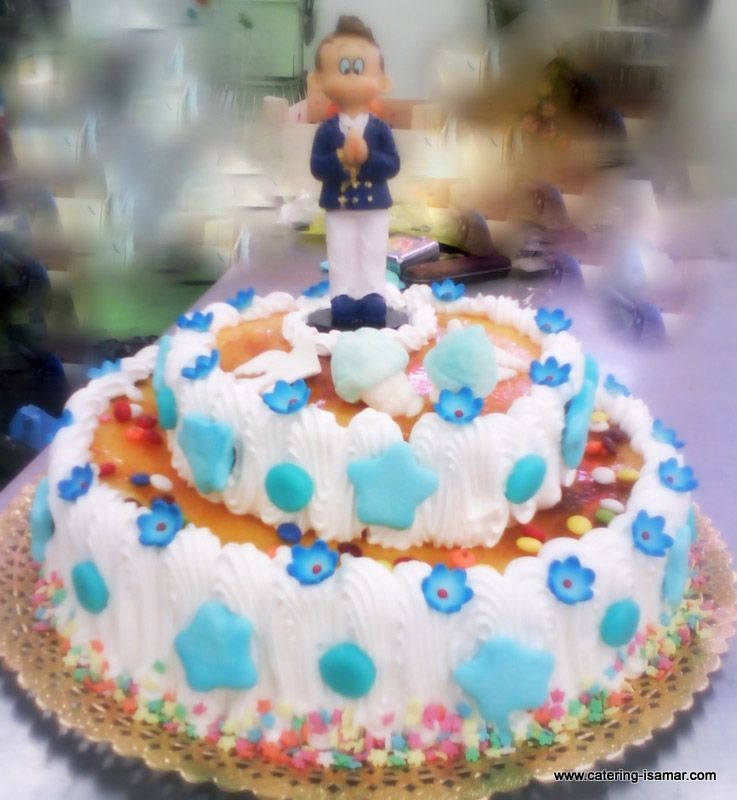 Tarta blanca de dos pisos con glaseado azul y naranja, chispas de colores y una pequeña figurita como adorno.