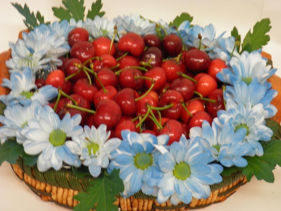 Cesta de cerezas rojas rodeada de flores azules y blancas.