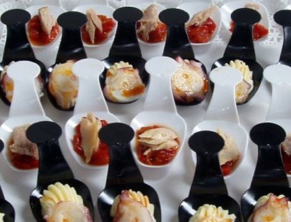 Filas de pequeñas cucharas de degustación con aperitivos cremosos y salsa roja en una bandeja.