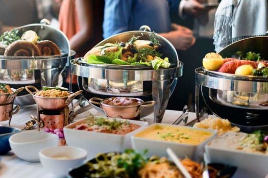 Mesa de buffet con platos cubiertos, ensaladas, fruta y bebidas en un evento con servicio de catering.