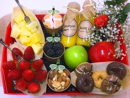 Surtido de frutas y dulces dispuestos en una bandeja de regalo con fresas, mango, manzanas y artículos cubiertos de chocolate.