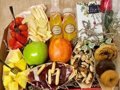 Surtido de frutas, frutos secos y aperitivos dispuestos en una cesta de regalo con dos botellas de zumo.