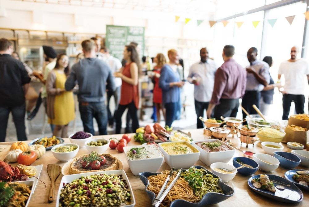 Servicio de catering tipo bufé con platos variados en una sala luminosa, con los invitados socializando al fondo.