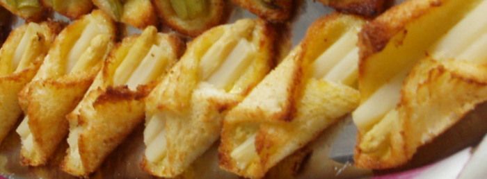 Primer plano de gajos de patata fritos dorados con un aderezo crujiente en un plato blanco.