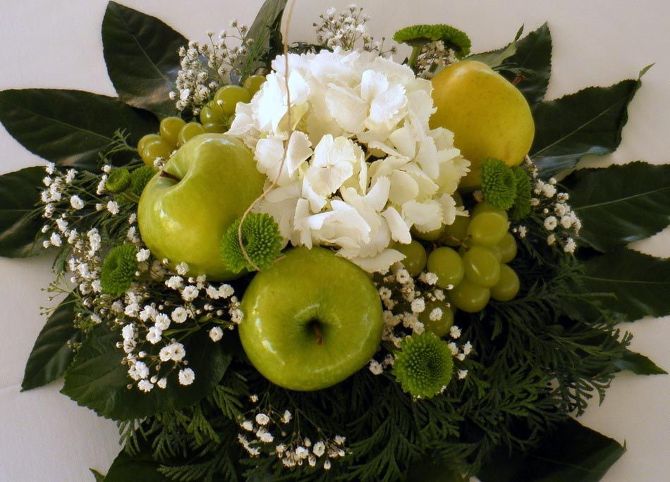 Manzanas verdes y flores blancas dispuestas en un centro de mesa floral decorativo.