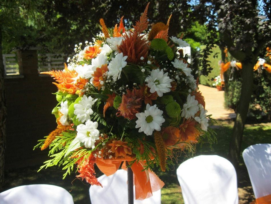 Arreglo floral blanco y naranja con cinta en un entorno de boda al aire libre.