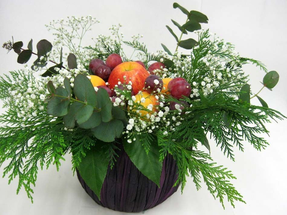 Arreglo floral de frutas y follaje otoñales en un jarrón redondo oscuro.