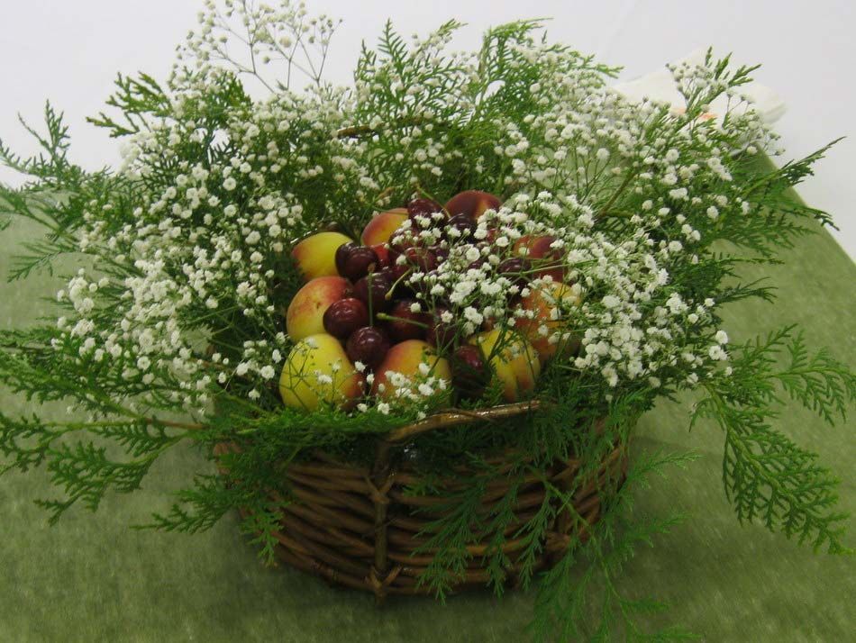 Cesta de fruta y flores blancas con hojas de helecho verdes sobre fondo de hierba.