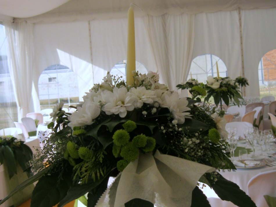 Centro de mesa floral blanco con follaje y cinta en un espacio para eventos decorado con carpa.